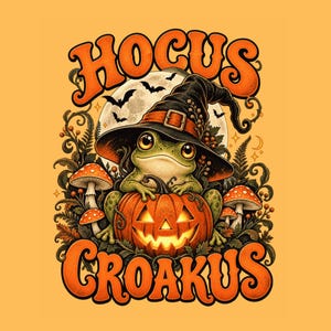May include: A graphic illustration featuring a green frog wearing a black witch hat, sitting on a glowing jack-o'-lantern. The design includes red and white mushrooms, bats, and a full moon, with the orange text HOCUS CROAKUS at the top and bottom.