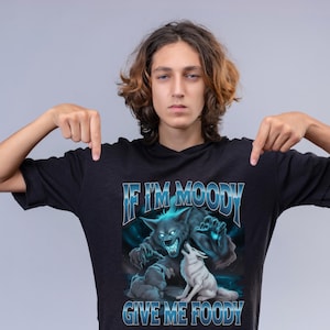 May include: Black t-shirt with a graphic featuring a snarling werewolf, two smaller wolves, and the text "IF I'M MOODY GIVE ME FOODY" in blue and white. The design has a fantasy theme.