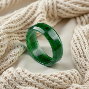 May include: A smooth, polished bangle bracelet crafted from deep green jade stone. The circular band features natural variations in color, ranging from dark forest green to lighter, translucent emerald tones with subtle black inclusions throughout.