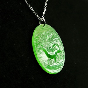 May include: A bright green oval pendant necklace with a detailed carved design of a dinosaur in a landscape. The pendant is suspended from a delicate silver chain, creating a striking contrast.