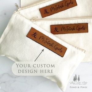 May include: Three white canvas zipper pouches with brown leather labels. The labels have the text "友 McIntosh Girls" on them. The bottom pouch has a space for a custom design.