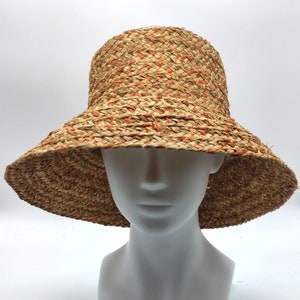 Könnte beinhalten: Ein breitkrempiger Strohhut mit einem gewebten Muster in Braun- und Orangetönen. Der Hut hat eine leicht abgerundete Krone und eine breite, weiche Krempe.