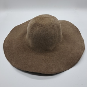 May include: A taupe-coloured hat with a wide brim. The hat features a rounded crown and a broad, floppy brim, made from a soft felt-like material. This hat is designed for sun protection and is suitable for outdoor wear.