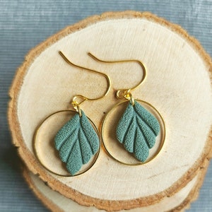 Könnte beinhalten: Ein Paar goldene Creolen mit einem tealgrünen Blatt-Anhänger an jedem Creolen.