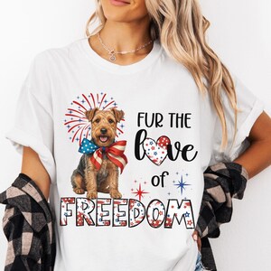 May include: White t-shirt featuring a dog with a patriotic bow tie, fireworks, and the text "FUR THE love of FREEDOM" in red, white, and blue. The shirt is a casual style, perfect for celebrating Independence Day.