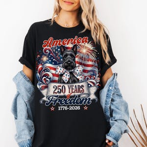 May include: Black t-shirt featuring a patriotic design with a Scottish Terrier dog wearing a bow. The graphic includes the word "America", an American flag, fireworks, and the text "250 Years of Freedom 1776-2026".