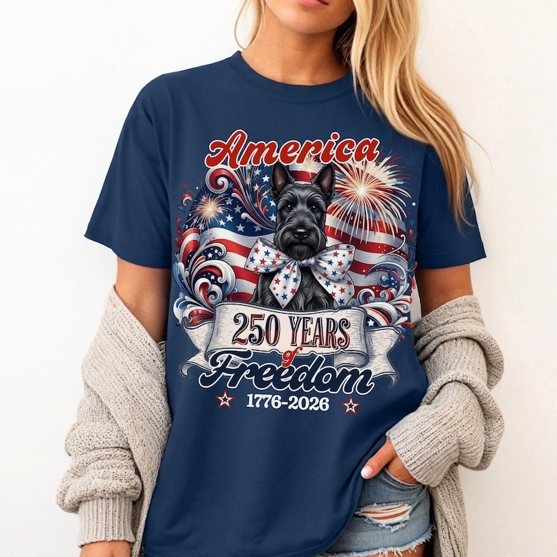May include: Navy blue t-shirt featuring a Scottish Terrier with a patriotic bow tie, the word "America" in red script, and a banner reading "250 Years of Freedom 1776-2026" with fireworks and an American flag design.