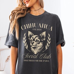 May include: A black t-shirt with a white graphic of a chihuahua dog. The graphic includes the text "Chihuahua Est 2024 Social Club Together for the Paws".
