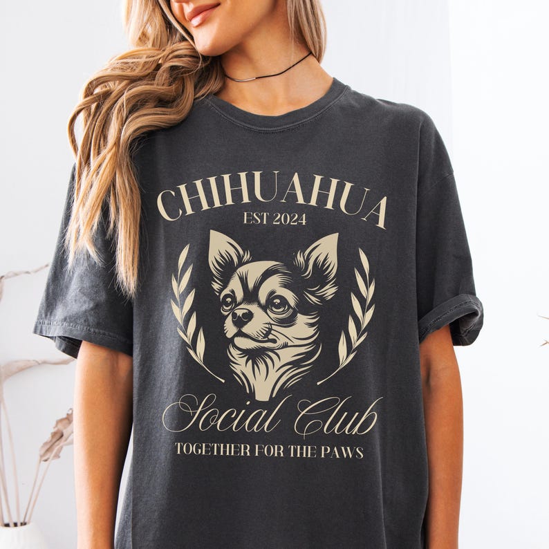 May include: A black t-shirt with a white graphic of a chihuahua dog. The graphic includes the text "Chihuahua Est 2024 Social Club Together for the Paws".
