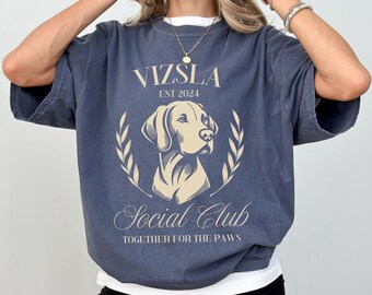 May include: A navy blue t-shirt featuring a graphic of a Vizsla dog and the text "Vizsla Est 2024 Social Club Together for the Paws".