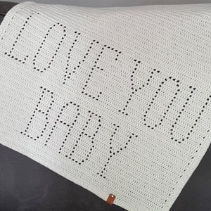 May include: White crocheted baby blanket with the words "Love You" in black yarn.