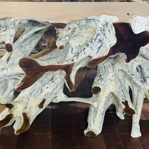 May include: A large, whitewashed, natural wood coffee table with a unique, organic shape. The table has a natural wood top and a base made of multiple branches that have been bleached white.