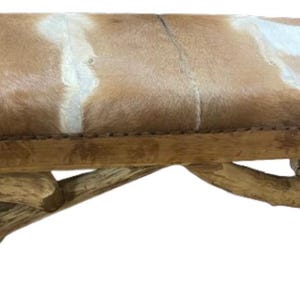 May include: A wooden bench with a unique, rustic design. The seat is covered in a brown and white animal hide.