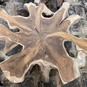 May include: A large, natural wood coffee table with a unique, organic shape and a rich brown color. The table has a live edge design and features a natural wood grain pattern.