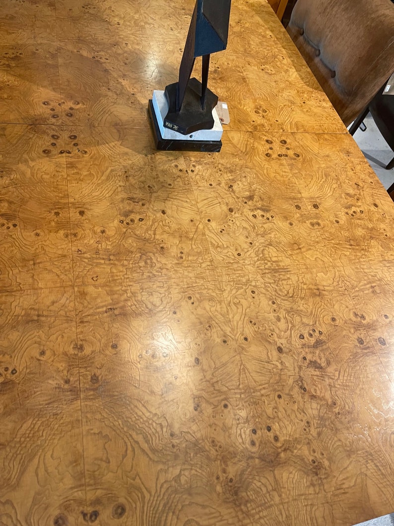 May include: A close-up of a wood table top with a burl wood veneer. The table top has a warm brown colour with a natural wood grain pattern. The table top is smooth and polished.