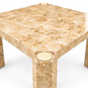 May include: A square table with a polished beige and tan mottled stone-like finish. The table features four thick legs, each topped with a circular inset disc. A small gold-toned metal pin is visible on the front leg, just below the circular disc.
