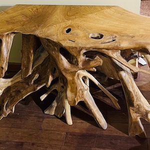 May include: A natural wood console table with a unique, organic shape. The table top is made of a single piece of wood with a natural, rustic finish. The legs are made of branches that have been carved and polished. The table is perfect for adding a touch of nature to any room.