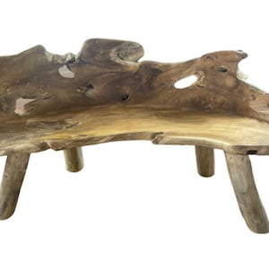 May include: A rustic wooden bench made from a single piece of reclaimed teak wood. The bench has a natural, organic shape with a curved seat and three legs. The wood is a rich brown color with a natural grain pattern.