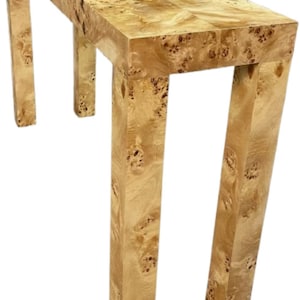 May include: A rectangular console table made of light-colored wood with a unique burl grain pattern. The table has four sturdy, angled legs and a long, flat top. The wood has a natural, warm tone.