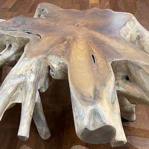 May include: A large, rustic wooden coffee table made from a tree root. The table has a natural, organic shape with a wide, flat top and several thick, gnarled legs. The wood is a rich brown color with a smooth, polished finish.