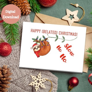 May include: A white card with a sloth hanging from a branch with Christmas lights. The card says "Happy (Belated) Christmas!" and "Ho Ho Slow" in red text.