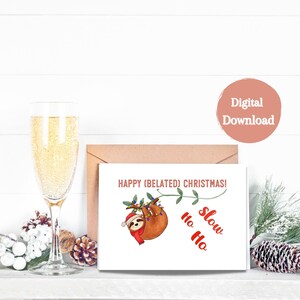 May include: A white card with a brown envelope behind it. The card has a cartoon sloth hanging from a branch with Christmas lights. The text on the card reads "Happy (Belated) Christmas! Ho Ho Slow".