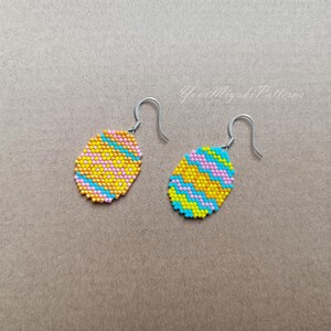 K&ouml;nnte beinhalten: Ein Paar Perlenohrringe mit einem gelben, rosa und blauen Muster. Die Ohrringe sind oval geformt und haben silberne Haken.