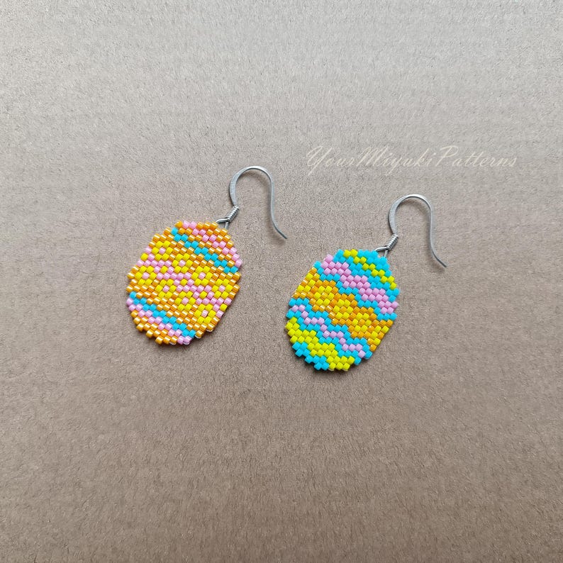 K&ouml;nnte beinhalten: Ein Paar Perlenohrringe mit einem gelben, rosa und blauen Muster. Die Ohrringe sind oval geformt und haben silberne Haken.