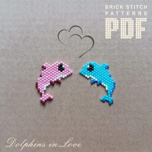 Könnte beinhalten: Zwei Perlen-Delfin-Figuren, eine rosa und eine blaue, die sich mit offenem Maul gegenüberstehen. Die Delfine sind in einer Sprungpose. Der Text "Dolphins in Love" befindet sich unter den Figuren. Der Text "BRICK STITCH PATTERNS PDF" befindet sich oben im Bild.