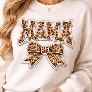 Könnte beinhalten: Cremefarbenes Sweatshirt mit dem Wort "MAMA" in brauner Leopardenmuster-Schrift. Eine passende Schleife mit Leopardenmuster befindet sich unter dem Text. Das Sweatshirt ist ein lässiger Stil, geeignet für den Alltag.