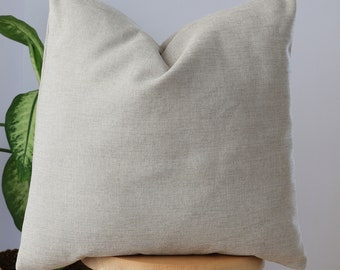 May include: A plain, light beige throw pillow with a linen texture sits on a wooden stool.
