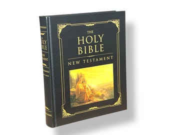 May include: A black hardback book titled "THE HOLY BIBLE NEW TESTAMENT." The book has gold lettering and decorative gold trim. The cover features a colour illustration of a person in a robe in a landscape.