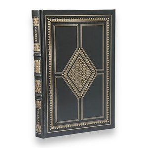 May include: A hardcover book with a black cover and gold-colored decorative accents. The spine reads "CANDIDE" and "VOLTAIRE" in gold lettering. The cover features a geometric design with a diamond-shaped pattern.