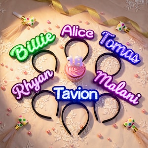 May include: Six black headbands featuring illuminated custom names in various colors including green, purple, and white, arranged around a single cupcake topped with a white candle shaped like the number 18, surrounded by party blowers and pearls.