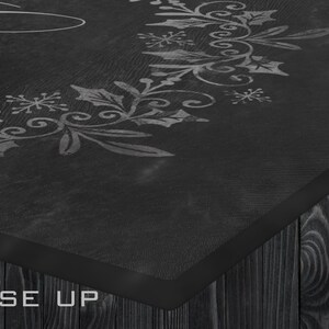 May include: Close-up of a black wooden sign with a white painted design of a wreath with holly leaves and snowflakes. The sign has a black border and the words "CLOSE UP" are printed in white at the bottom.