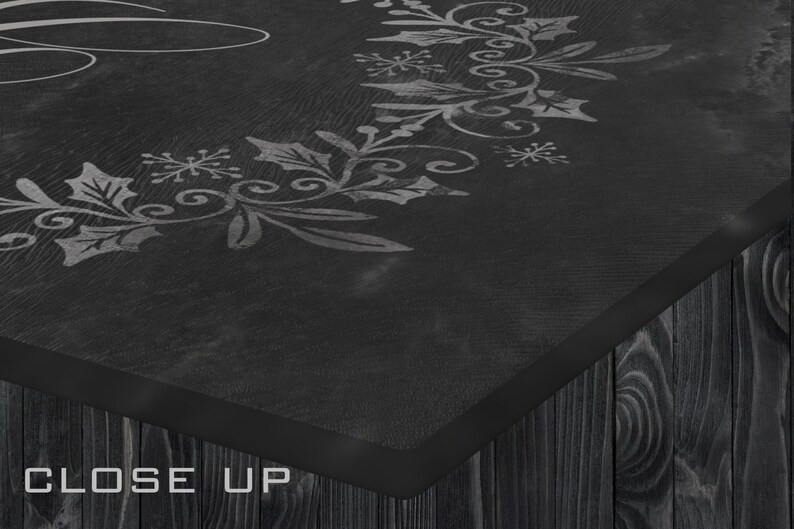 May include: Close-up of a black wooden sign with a white painted design of a wreath with holly leaves and snowflakes. The sign has a black border and the words "CLOSE UP" are printed in white at the bottom.