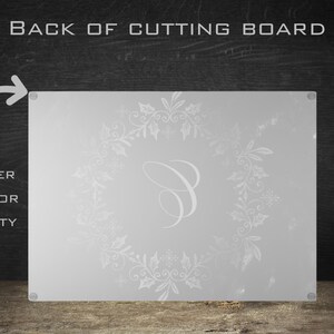 May include: White glass cutting board with a white snowflake and floral design and a letter "C" in the center. The back of the board has rubber dots for stability.