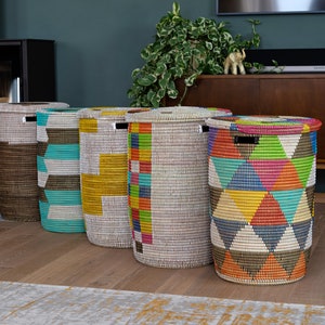 Puede incluir: Cinco cestos de lavander&iacute;a cil&iacute;ndricos altos con tapas. Las cestas est&aacute;n hechas de material tejido y presentan patrones geom&eacute;tricos coloridos en turquesa, amarillo, rojo y otros colores. Est&aacute;n colocados sobre un suelo de madera.