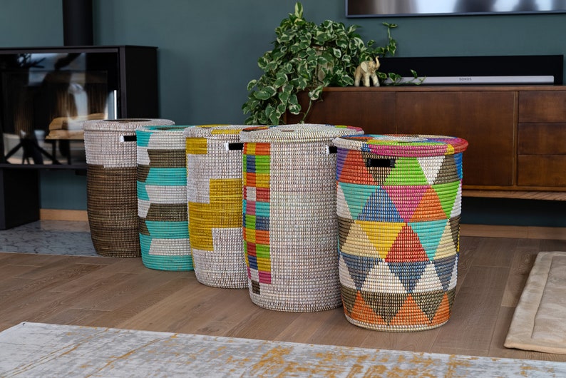 Puede incluir: Cinco cestos de lavander&iacute;a cil&iacute;ndricos altos con tapas. Las cestas est&aacute;n hechas de material tejido y presentan patrones geom&eacute;tricos coloridos en turquesa, amarillo, rojo y otros colores. Est&aacute;n colocados sobre un suelo de madera.