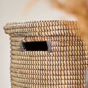 May include: A woven storage basket with black and natural colored stripes. The basket has a rectangular opening on the side.