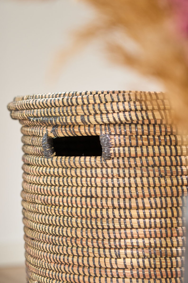 May include: A woven storage basket with black and natural colored stripes. The basket has a rectangular opening on the side.