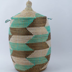 Puede incluir: Una cesta de almacenamiento grande y tejida con tapa. La cesta est&aacute; hecha de materiales naturales y tiene un patr&oacute;n geom&eacute;trico en tonos marrones, blancos y turquesa.