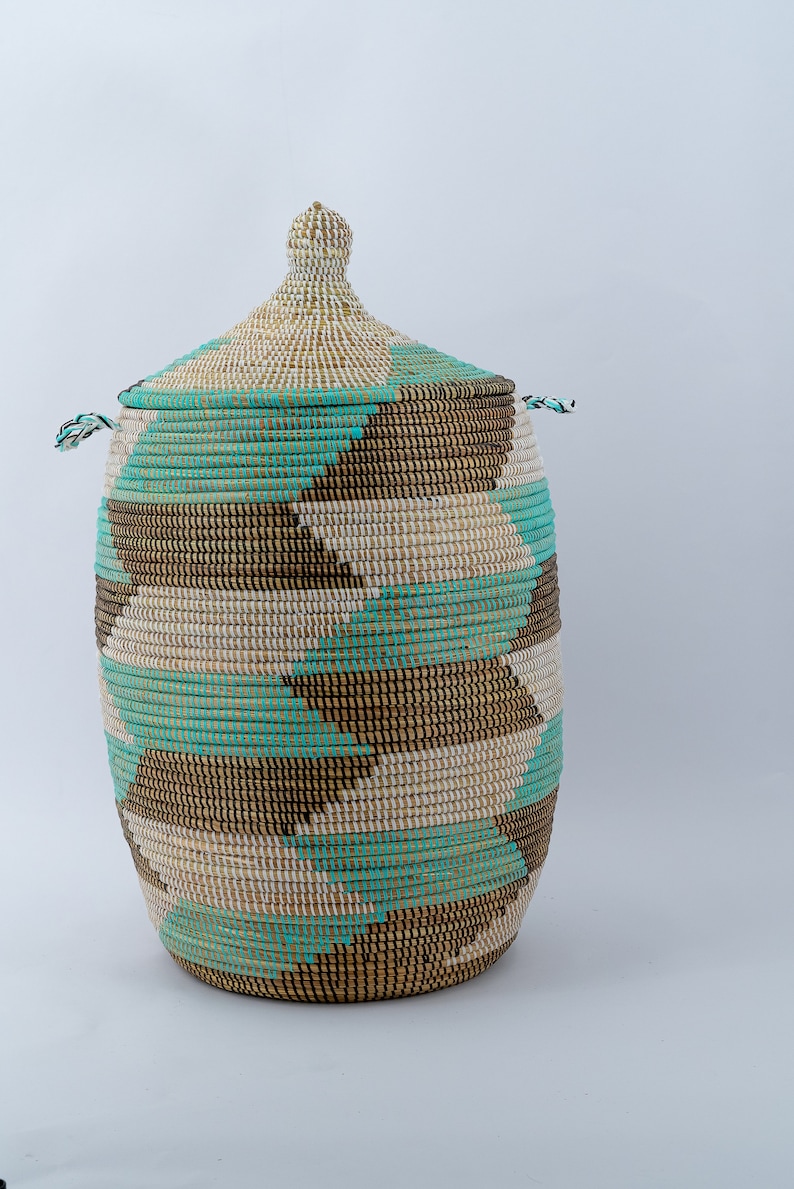 Puede incluir: Una cesta de almacenamiento grande y tejida con tapa. La cesta est&aacute; hecha de materiales naturales y tiene un patr&oacute;n geom&eacute;trico en tonos marrones, blancos y turquesa.