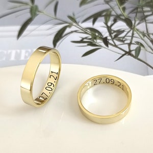 Könnte beinhalten: Zwei goldene Eheringe mit der Gravur "27.09.21" auf der Innenseite jedes Rings.