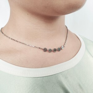 May include: A silver chain necklace with a pendant that spells out the word "BRAVE" in individual silver circles.