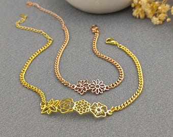 May include: Two delicate gold-colored chain bracelets. One features a series of openwork flower designs, while the other has two flower designs. The bracelets are displayed on a gray surface.