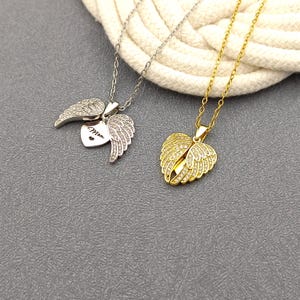 May include: Two silver and gold necklaces with angel wing pendants. The silver pendant has a heart with the word "Mom" inscribed on it. Both pendants are adorned with clear cubic zirconia stones.