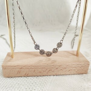 May include: A silver chain necklace with a pendant that spells out the word "BRAVE" in individual silver circles.