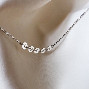 May include: A silver chain necklace with round silver charms spelling out the word "LUCKY".