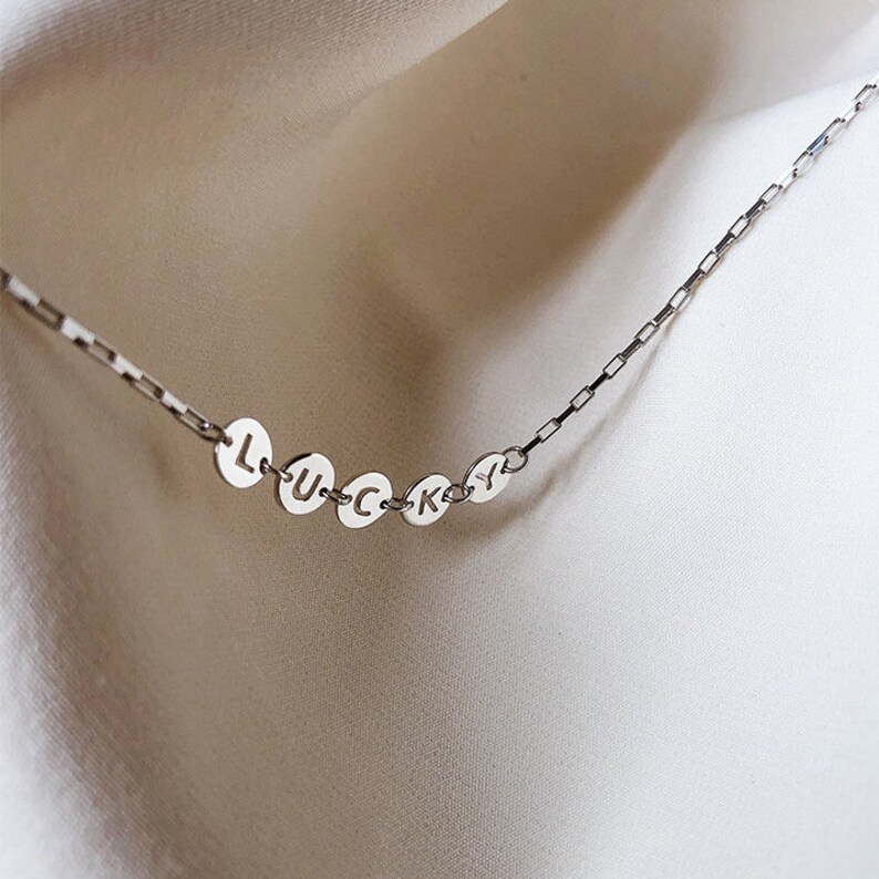 May include: A silver chain necklace with round silver charms spelling out the word "LUCKY".
